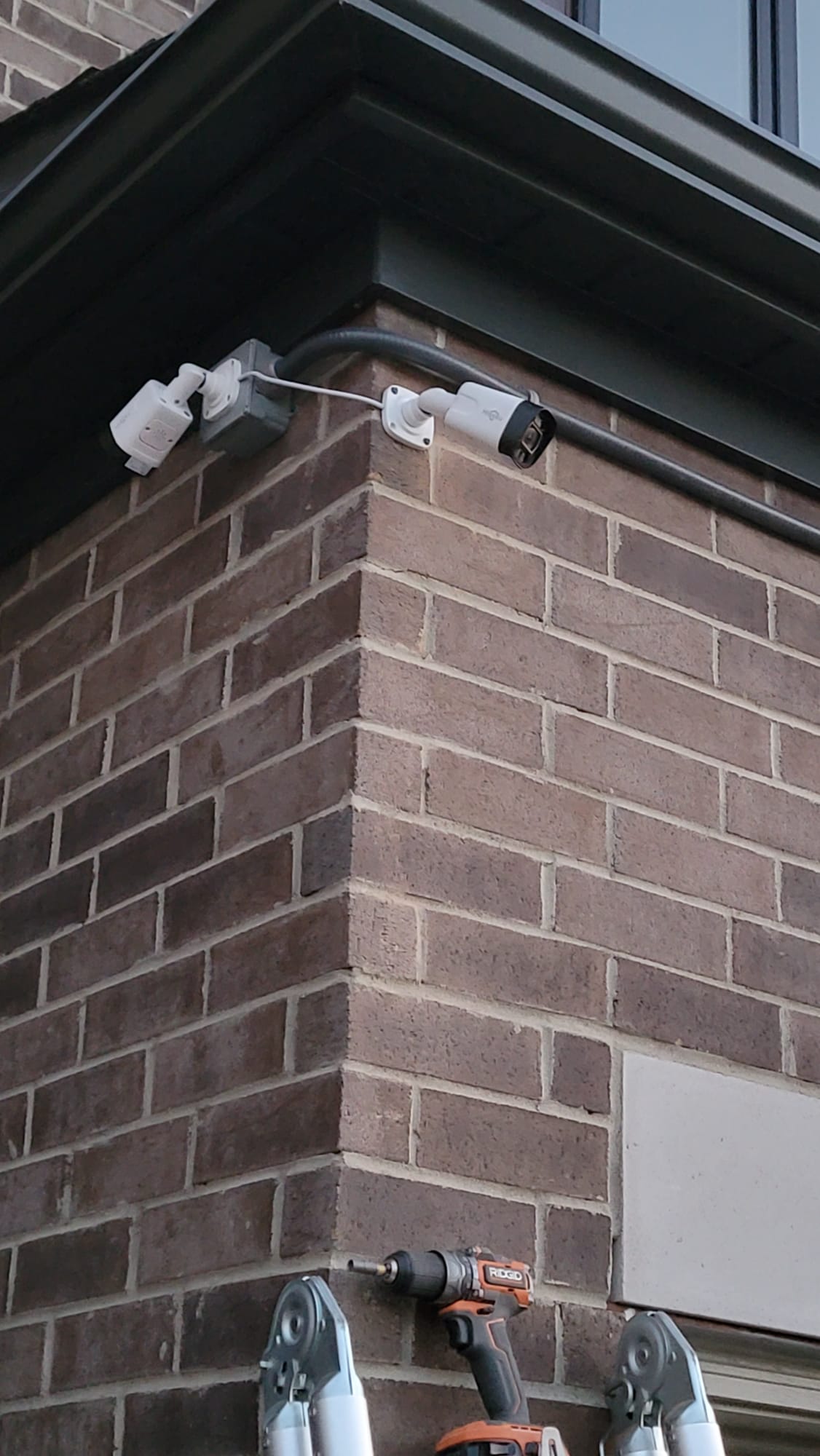 Corner-mounted bullet CCTV camera and floodlight cleanly installed on brick exterior wall
