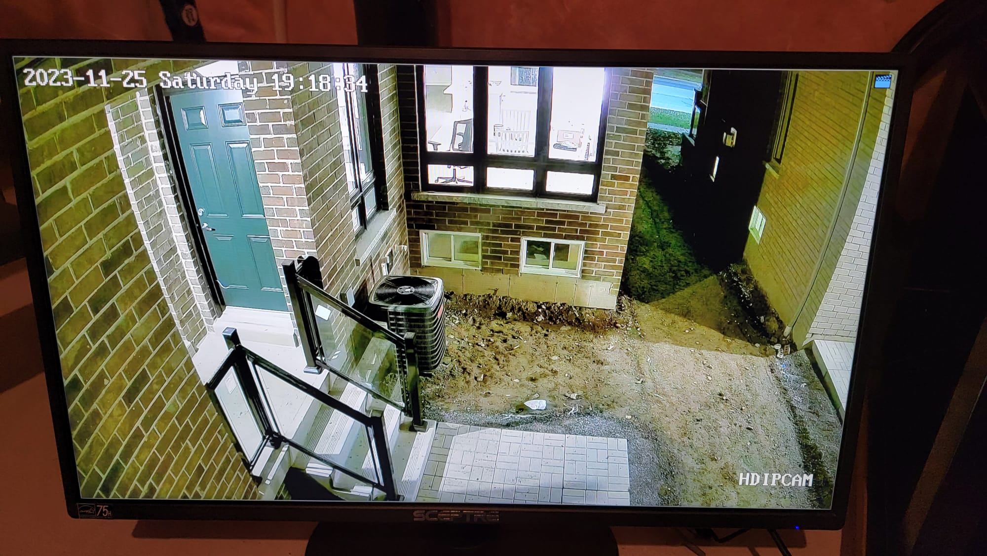 CCTV monitor showing residential front entrance area with HVAC unit and walkway visible