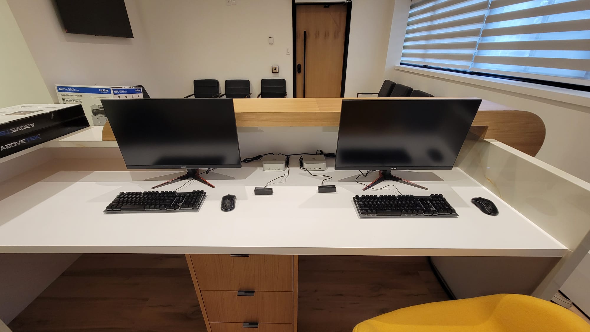 Dual-monitor reception workstation with mechanical keyboards, mini PCs, and printer in finished medical office