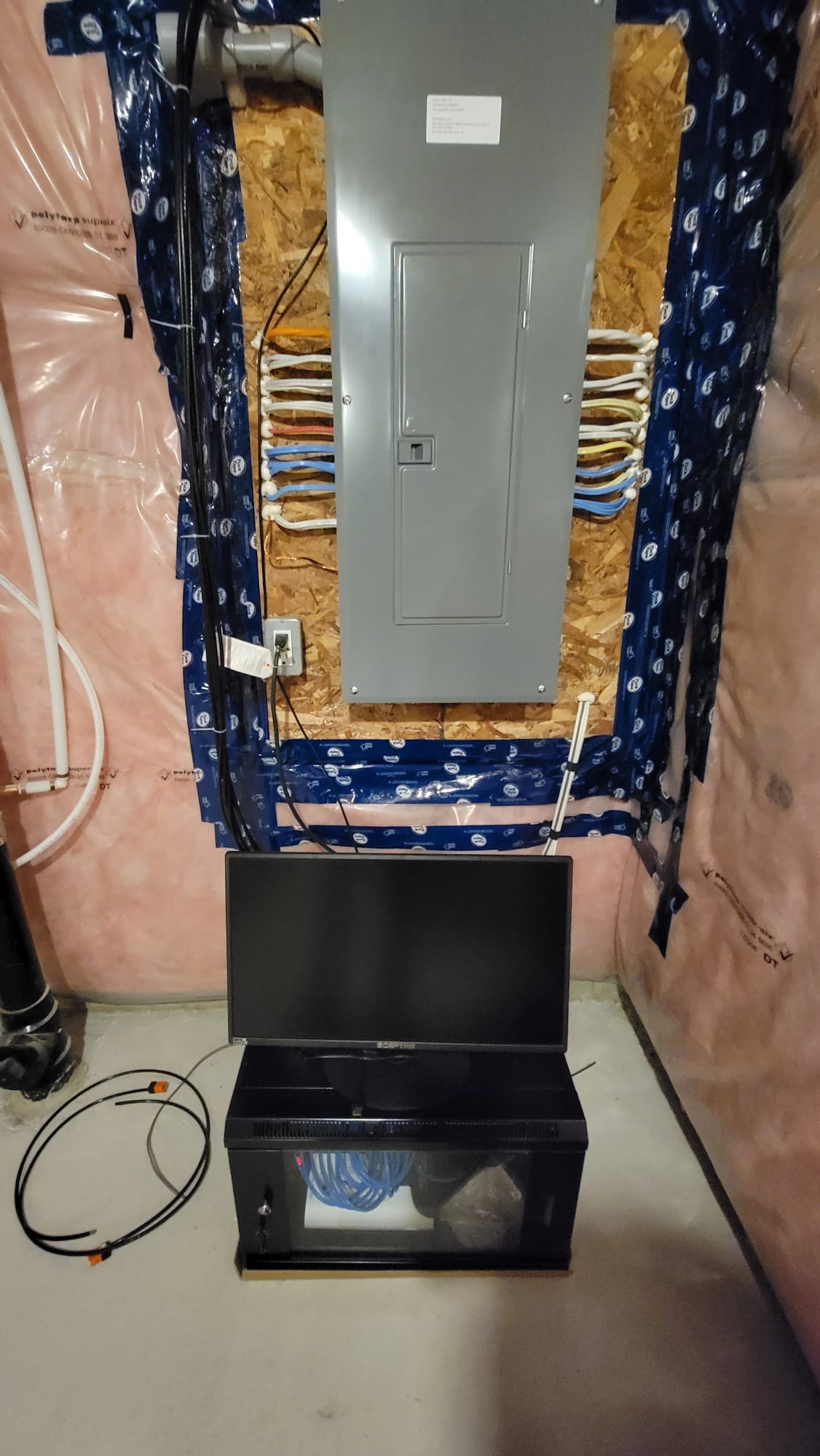 Utility wall with electrical panel and structured network cabling above wall-mount cabinet and monitor