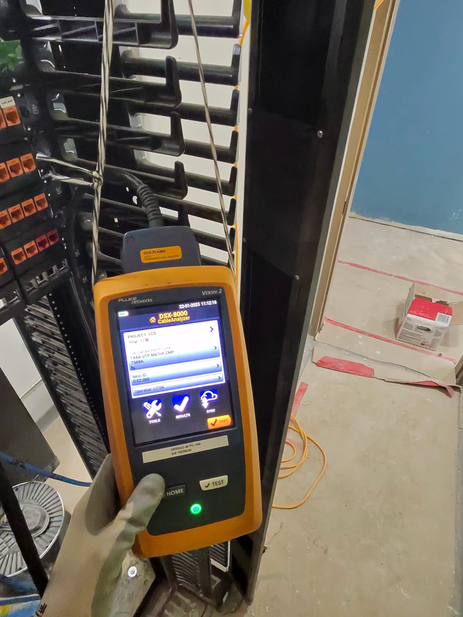 Gloved hand holding Fluke DSX-8000 CableAnalyzer running certification test at structured cabling rack
