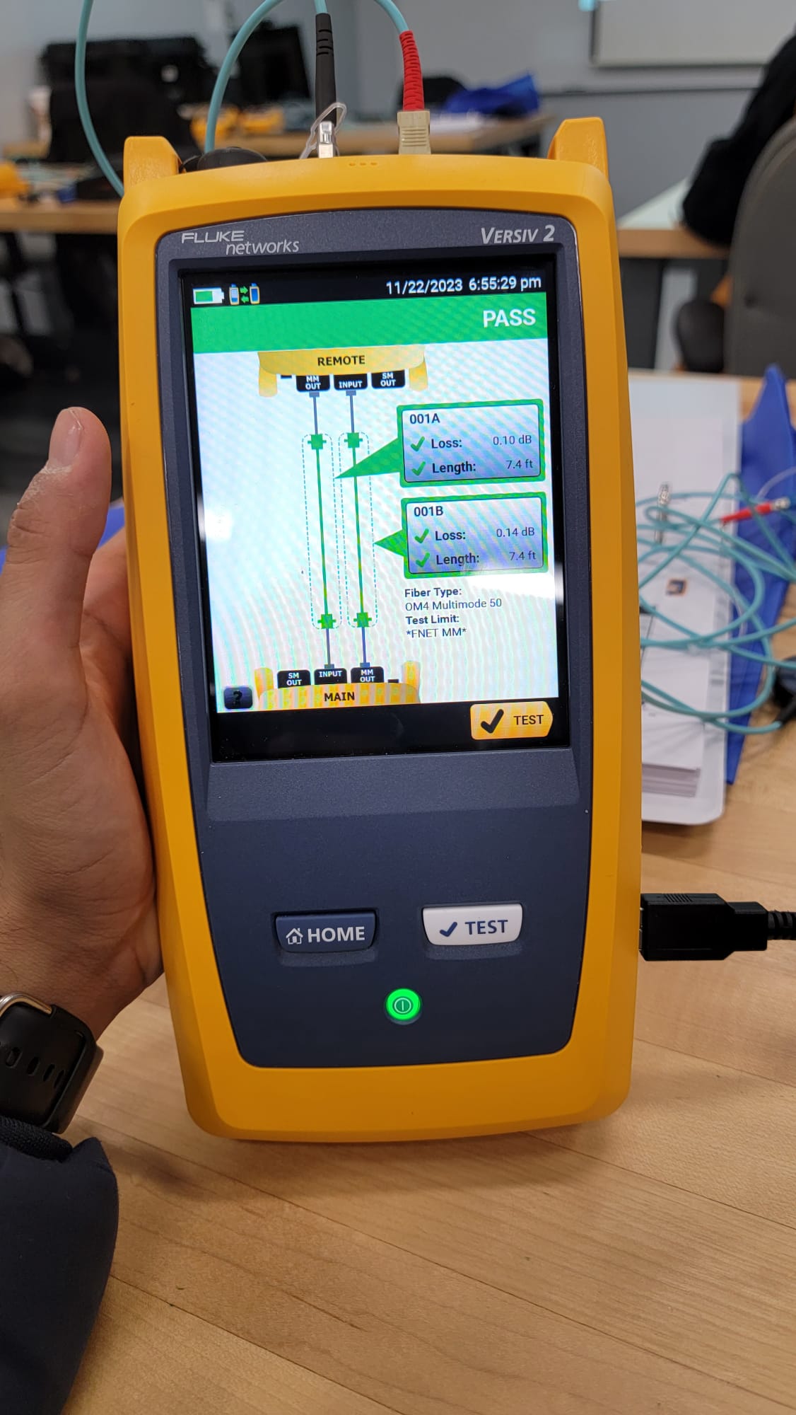 Hand holding Fluke Versiv 2 displaying PASS result on OM4 multimode 50 fiber certification test