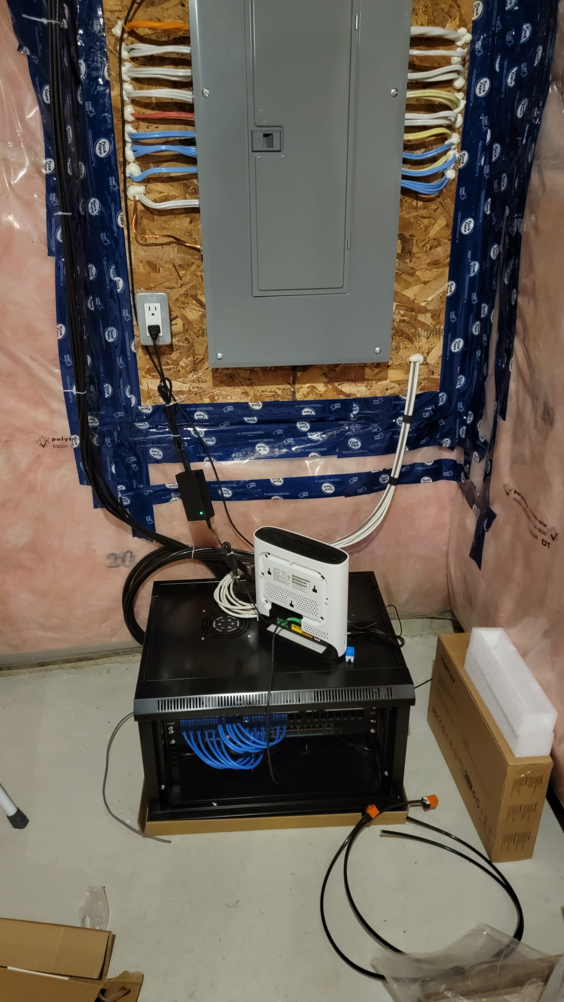 Wall-mount network cabinet with coiled blue Cat6 cabling beneath the electrical panel during basement structured wiring rough-in