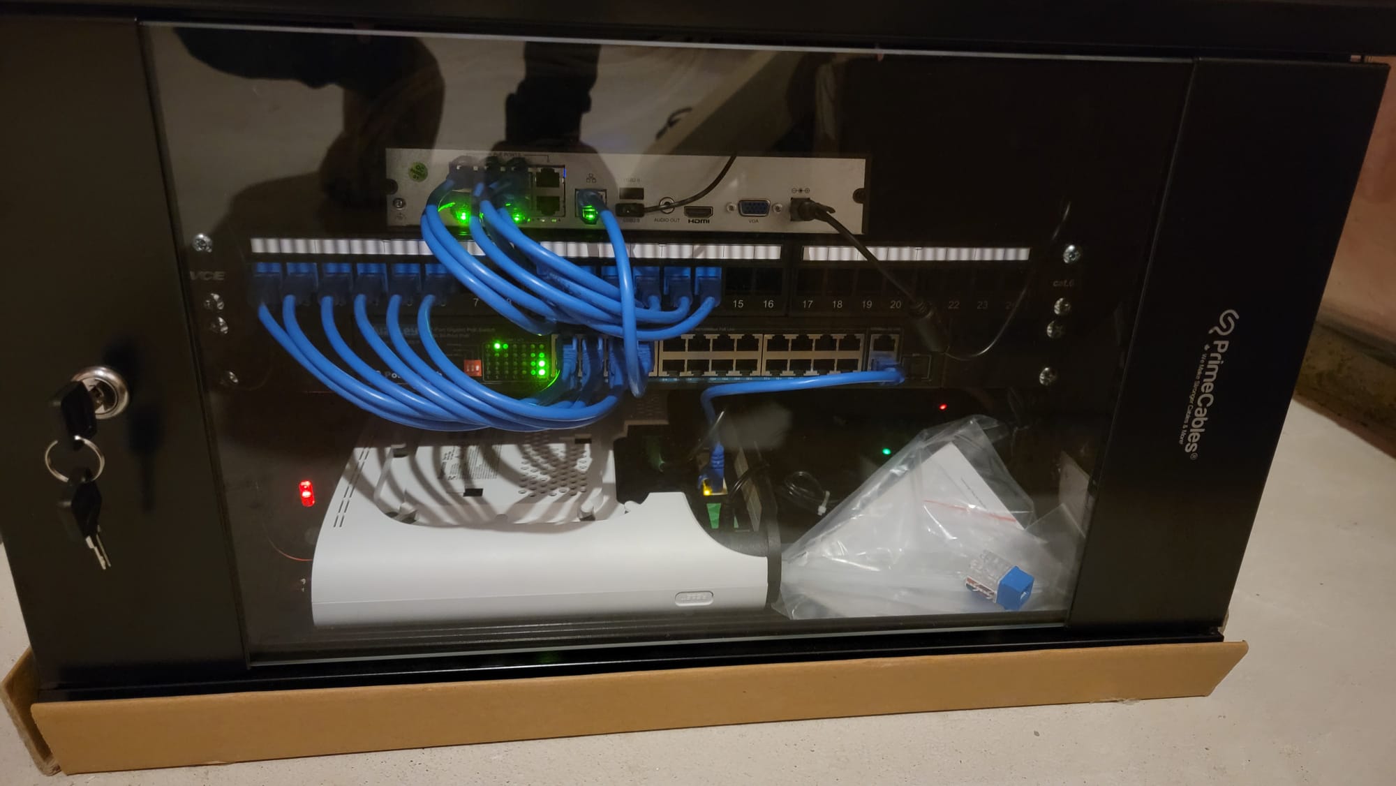 Open network cabinet showing PoE switch, patch panel, and NVR with neatly coiled blue Cat6 patch cables