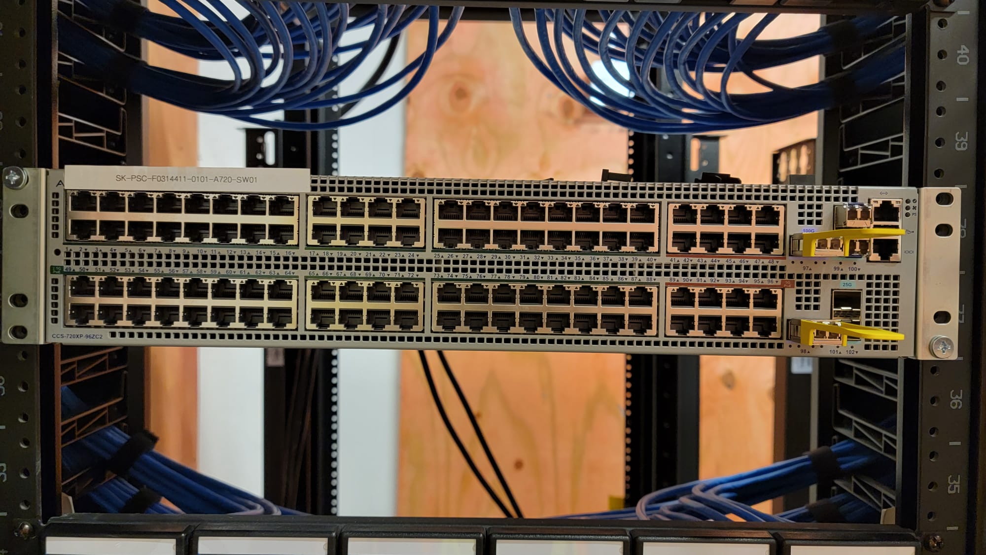 Two stacked 48-port enterprise network switches with blue Cat6 patch cables routed above and below in dark equipment rack